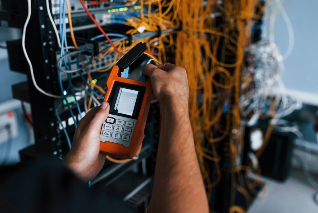 Young man withj measuring device in hands works with internet equipment and wires in server room